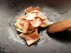 にんにくを炒めているフライパンに玉ねぎとベーコンを入れる。