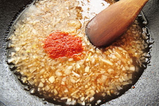 海南鶏飯のタレの材料を煮込んでいるフライパンに、一味唐辛子をくわえる。