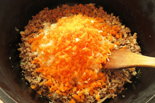 ひき肉を炒めている鍋に玉ねぎとにんじんを入れる。